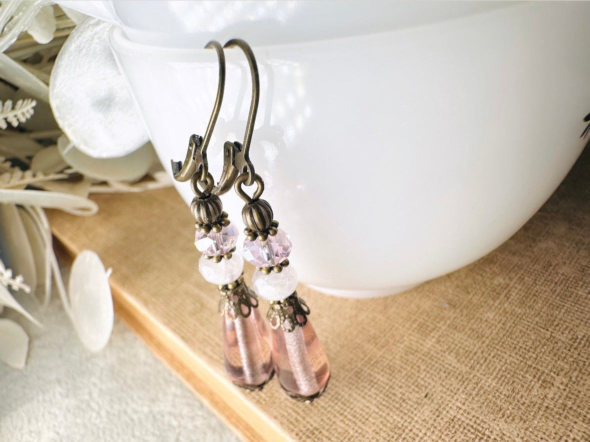These beautiful Victorian earrings are handmade with rose quartz stones, lustrous pink Czech glass teardrop beads, and faceted crystals. These whimsical blushing rose earrings feature a delightful mix of soft pink hues and rustic bronze detailing. A wonderful pair of earrings for elegant everyday wear.
