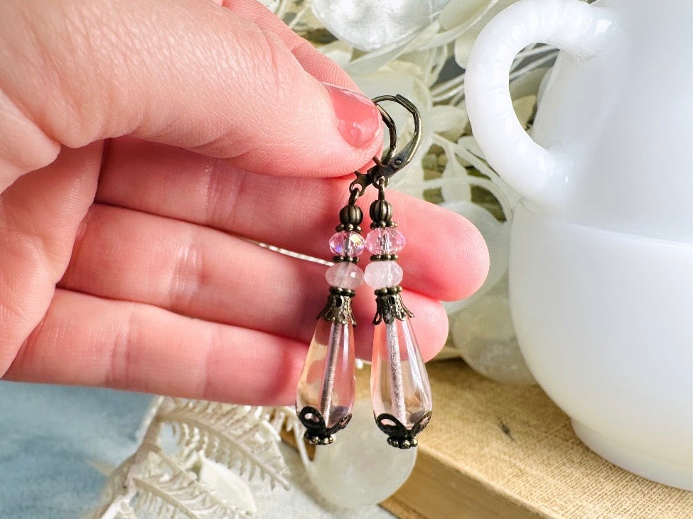 These beautiful Victorian earrings are handmade with rose quartz stones, lustrous pink Czech glass teardrop beads, and faceted crystals. These whimsical blushing rose earrings feature a delightful mix of soft pink hues and rustic bronze detailing. A wonderful pair of earrings for elegant everyday wear.