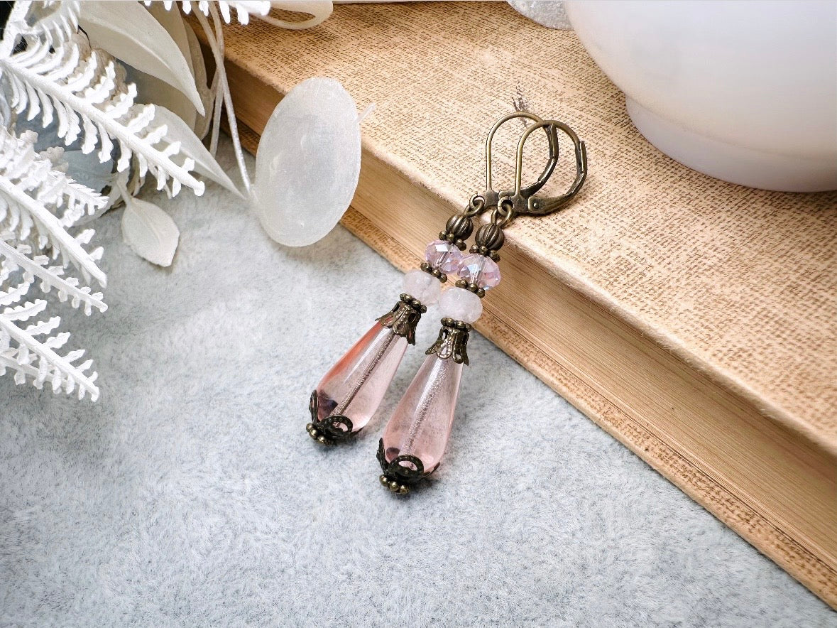 These beautiful Victorian earrings are handmade with rose quartz stones, lustrous pink Czech glass teardrop beads, and faceted crystals. These whimsical blushing rose earrings feature a delightful mix of soft pink hues and rustic bronze detailing. A wonderful pair of earrings for elegant everyday wear.