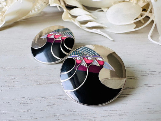 A pair of Laurel Burch vintage earrings titled  "Celestial Birds". These post earrings are shiny silver with black and plum pink enamel of three birds lined up in a side profile. Laurel Burch is highly collectible, and these are so unique. Engraved with the the title "Celestial Birds" on the back of earrings along the the signature on the backs. Silver plated posts, excellent condition with very minor wear. They are about 1 inch big and available from Piggle and Pop.