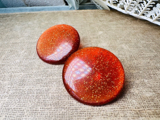 These vintage lucite button earrings from Piggle and Pop are such a gorgeous color- vibrant copper with flecks of fine gold glitter. These retro clip ons are from the 1960s. A fun party pair, these confetti earrings were wildly popular at the time and a fun statement pair to rock in modern day. Lightweight for their size, a round slightly domed coin shape and easy to wear in clip on style. They catch the light beautifully and can appear a deep reddish copper shade to a glowing sunset hue. 