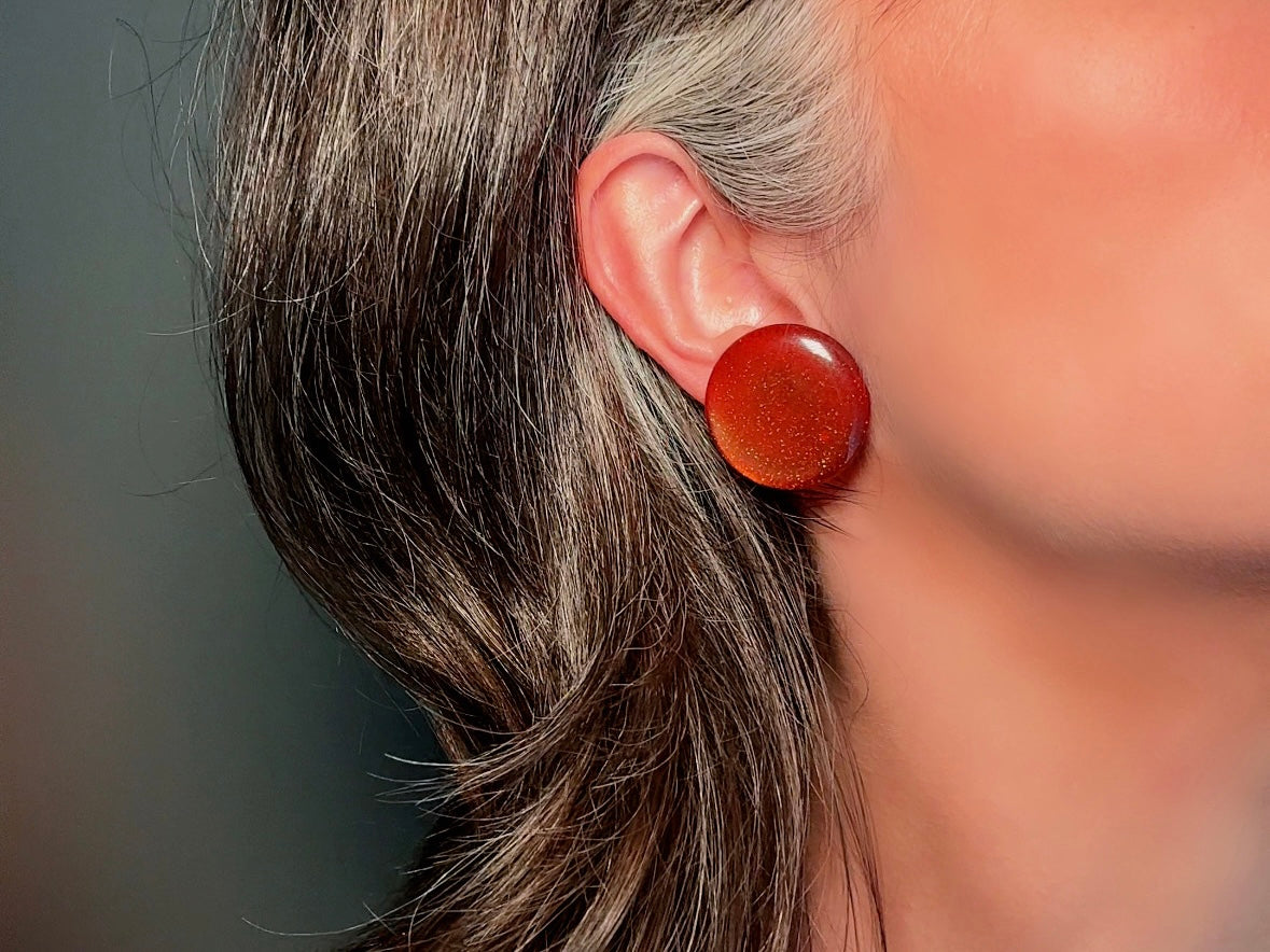 These vintage lucite button earrings from Piggle and Pop are such a gorgeous color- vibrant copper with flecks of fine gold glitter. These retro clip ons are from the 1960s. A fun party pair, these confetti earrings were wildly popular at the time and a fun statement pair to rock in modern day. Lightweight for their size, a round slightly domed coin shape and easy to wear in clip on style. They catch the light beautifully and can appear a deep reddish copper shade to a glowing sunset hue. 