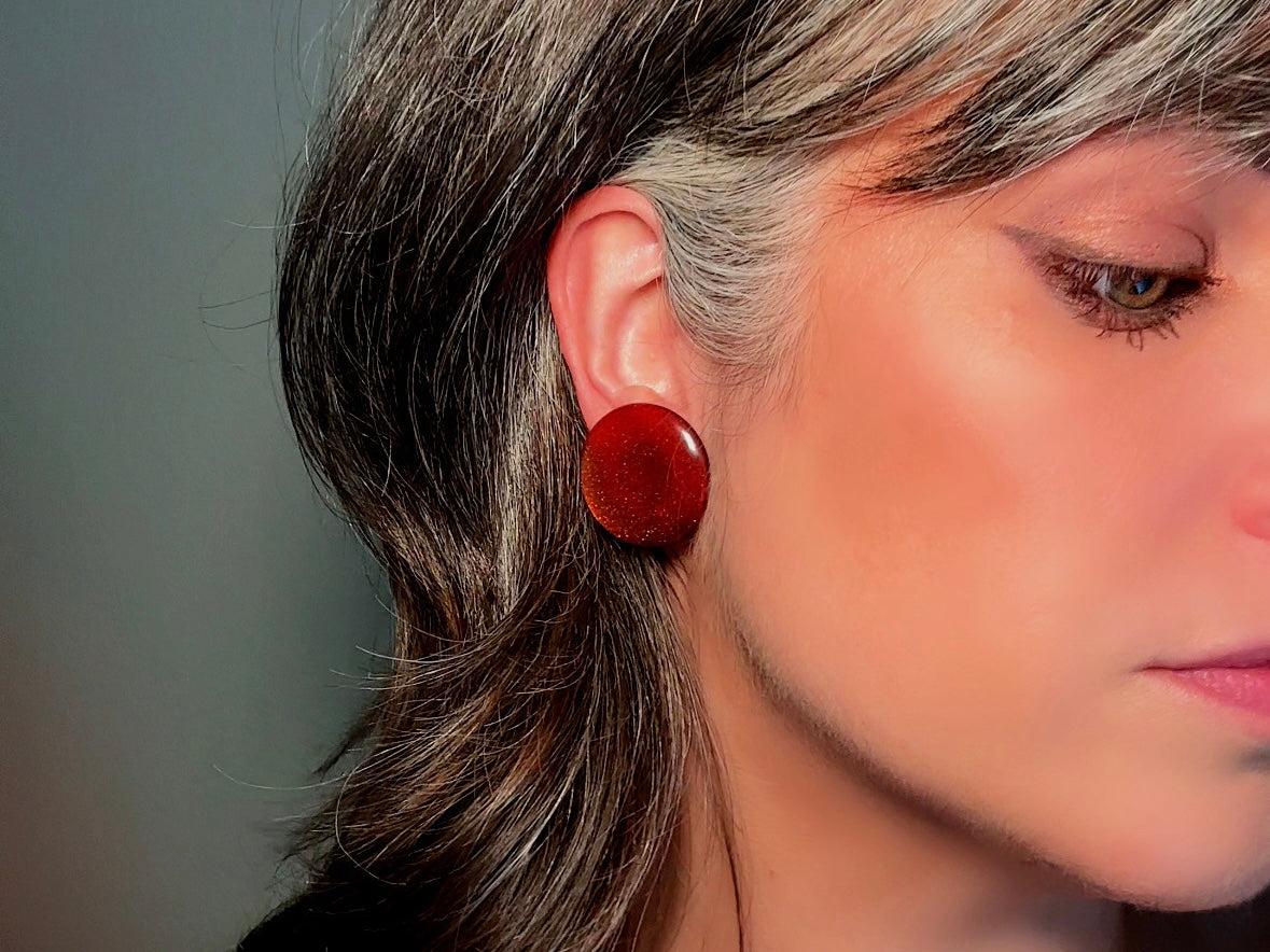 These vintage lucite button earrings from Piggle and Pop are such a gorgeous color- vibrant copper with flecks of fine gold glitter. These retro clip ons are from the 1960s. A fun party pair, these confetti earrings were wildly popular at the time and a fun statement pair to rock in modern day. Lightweight for their size, a round slightly domed coin shape and easy to wear in clip on style. They catch the light beautifully and can appear a deep reddish copper shade to a glowing sunset hue. 