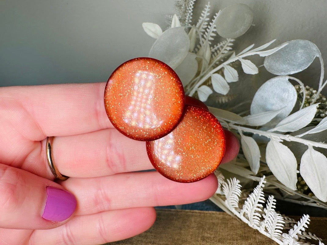 These vintage lucite button earrings from Piggle and Pop are such a gorgeous color- vibrant copper with flecks of fine gold glitter. These retro clip ons are from the 1960s. A fun party pair, these confetti earrings were wildly popular at the time and a fun statement pair to rock in modern day. Lightweight for their size, a round slightly domed coin shape and easy to wear in clip on style. They catch the light beautifully and can appear a deep reddish copper shade to a glowing sunset hue. 