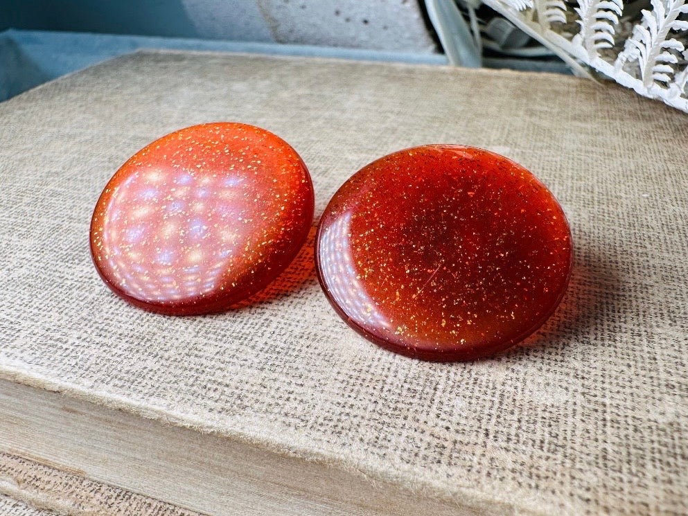 These vintage lucite button earrings from Piggle and Pop are such a gorgeous color- vibrant copper with flecks of fine gold glitter. These retro clip ons are from the 1960s. A fun party pair, these confetti earrings were wildly popular at the time and a fun statement pair to rock in modern day. Lightweight for their size, a round slightly domed coin shape and easy to wear in clip on style. They catch the light beautifully and can appear a deep reddish copper shade to a glowing sunset hue. 