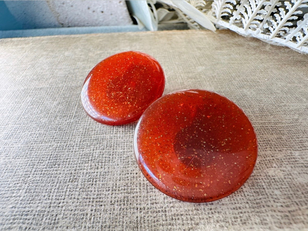These vintage lucite button earrings from Piggle and Pop are such a gorgeous color- vibrant copper with flecks of fine gold glitter. These retro clip ons are from the 1960s. A fun party pair, these confetti earrings were wildly popular at the time and a fun statement pair to rock in modern day. Lightweight for their size, a round slightly domed coin shape and easy to wear in clip on style. They catch the light beautifully and can appear a deep reddish copper shade to a glowing sunset hue. 