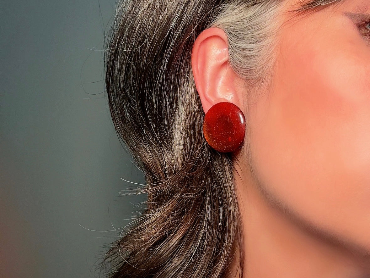 These vintage lucite button earrings from Piggle and Pop are such a gorgeous color- vibrant copper with flecks of fine gold glitter. These retro clip ons are from the 1960s. A fun party pair, these confetti earrings were wildly popular at the time and a fun statement pair to rock in modern day. Lightweight for their size, a round slightly domed coin shape and easy to wear in clip on style. They catch the light beautifully and can appear a deep reddish copper shade to a glowing sunset hue. 