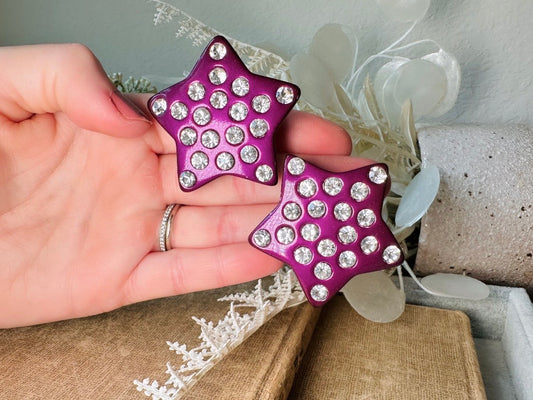 These oversized vintage purple star earrings are a highly collectible pair of 1980s statement earrings. These big and bold star earrings are a stunning shade of vibrant metallic magenta purple lucite with diamond rhinestone accents. Huge vintage star clip ons with major rockstar vibes. A fun 80s pair of unique earrings that you never knew you needed so badly.