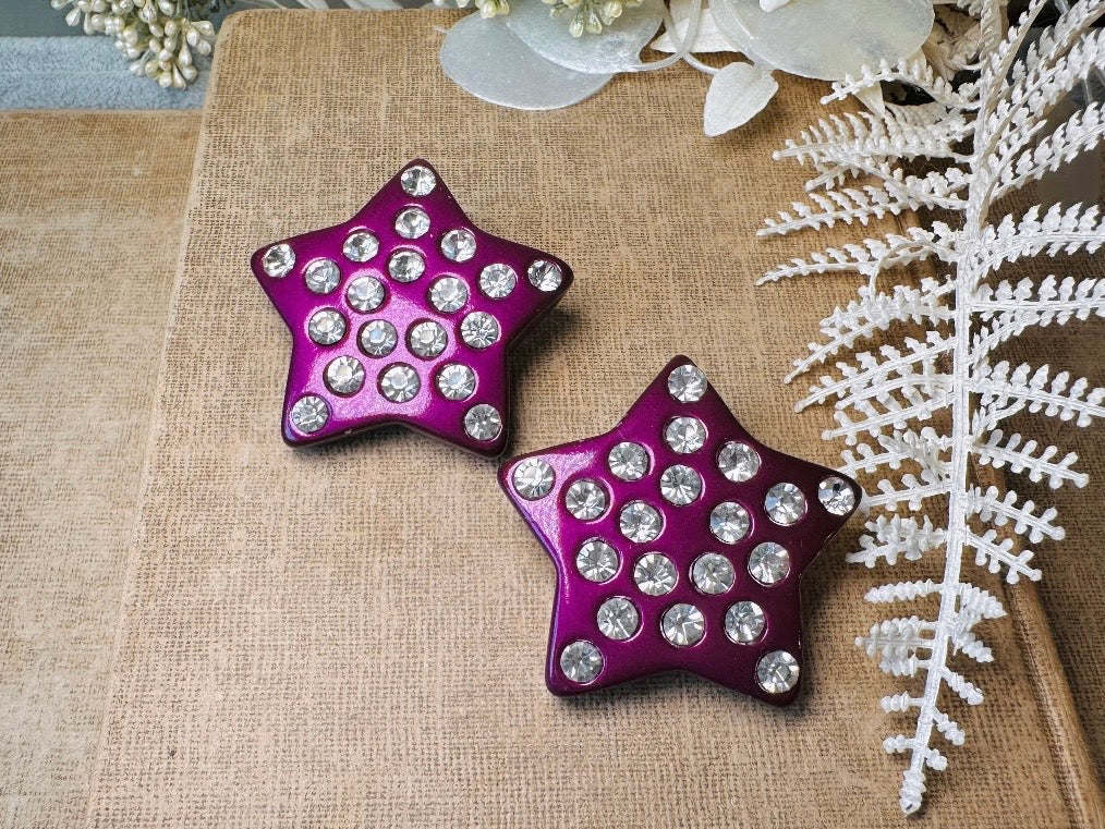 These oversized vintage purple star earrings are a highly collectible pair of 1980s statement earrings. These big and bold star earrings are a stunning shade of vibrant metallic magenta purple lucite with diamond rhinestone accents. Huge vintage star clip ons with major rockstar vibes. A fun 80s pair of unique earrings that you never knew you needed so badly.