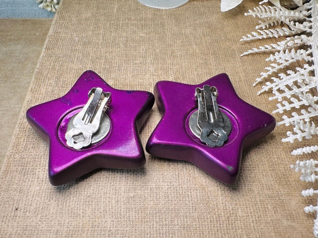 These oversized vintage purple star earrings are a highly collectible pair of 1980s statement earrings. These big and bold star earrings are a stunning shade of vibrant metallic magenta purple lucite with diamond rhinestone accents. Huge vintage star clip ons with major rockstar vibes. A fun 80s pair of unique earrings that you never knew you needed so badly.