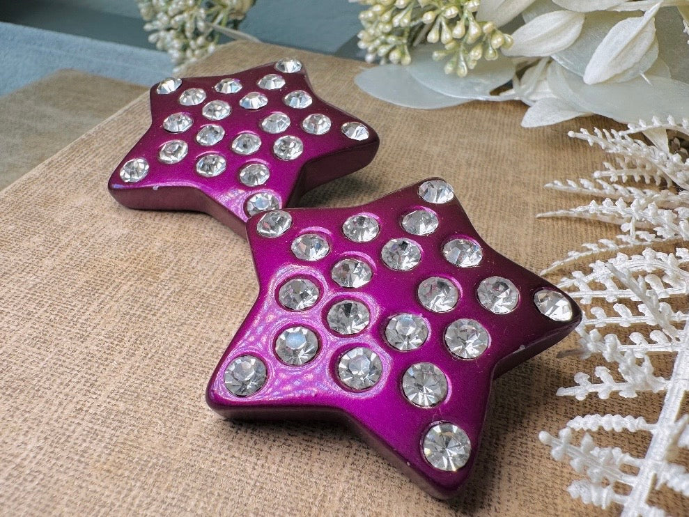 These oversized vintage purple star earrings are a highly collectible pair of 1980s statement earrings. These big and bold star earrings are a stunning shade of vibrant metallic magenta purple lucite with diamond rhinestone accents. Huge vintage star clip ons with major rockstar vibes. A fun 80s pair of unique earrings that you never knew you needed so badly.