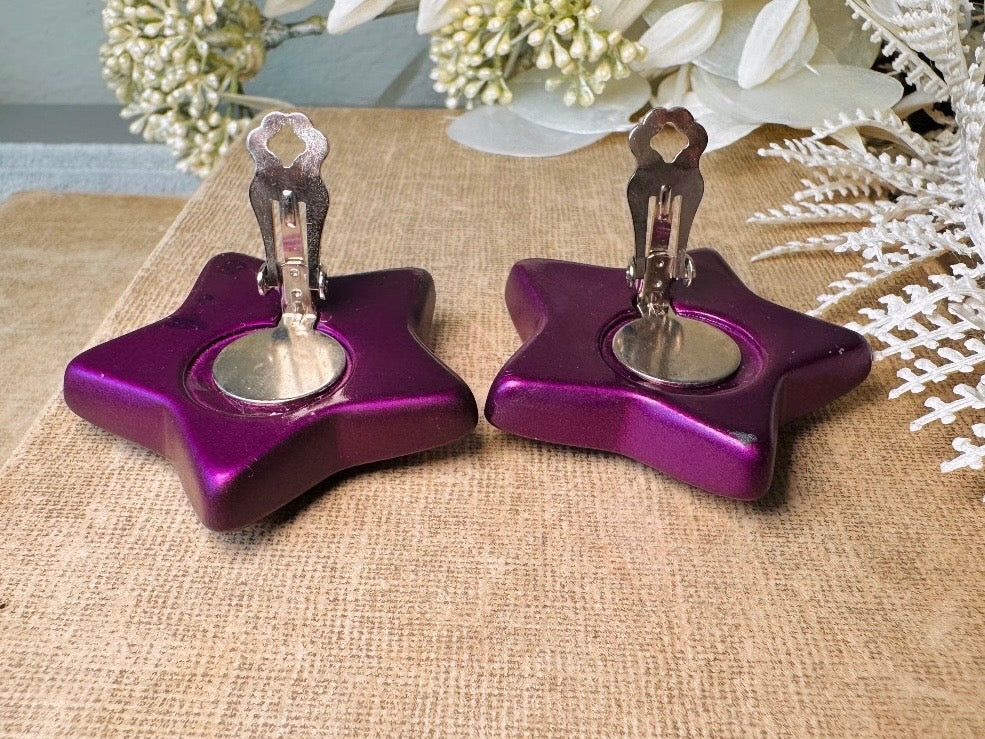 These oversized vintage purple star earrings are a highly collectible pair of 1980s statement earrings. These big and bold star earrings are a stunning shade of vibrant metallic magenta purple lucite with diamond rhinestone accents. Huge vintage star clip ons with major rockstar vibes. A fun 80s pair of unique earrings that you never knew you needed so badly.