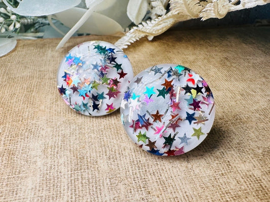 These vintage rainbow glitter button earrings from Piggle and Pop are such a fun party pair! These retro clip ons are from the 1980s, featuring clear domed lucite over a white background- the star confetti pops in such a cool way- metallic star glitter in teal, blue, yellow, red, gold, silver and green! A fun and carefree pair, these confetti earrings were wildly popular at the time and a fun statement pair to rock in modern day.