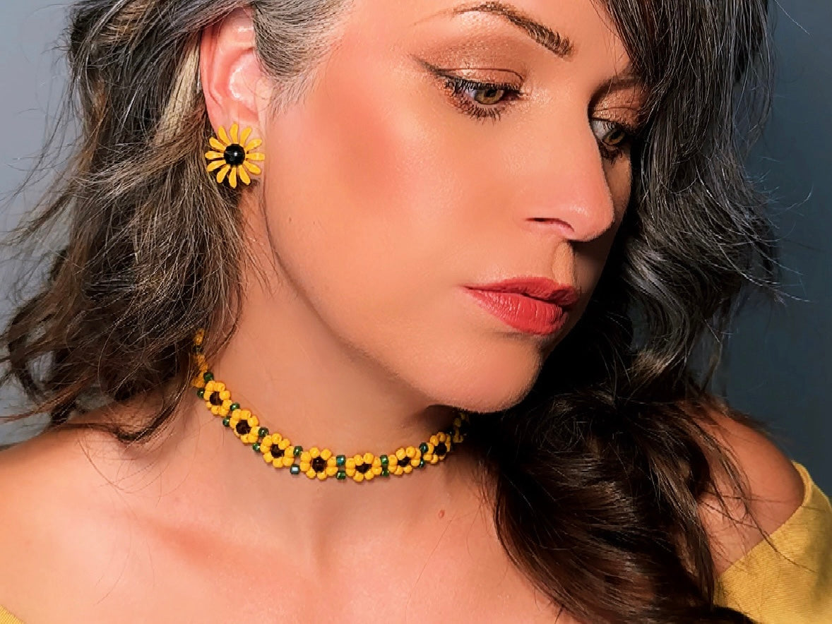 A close-up lifestyle shot of a woman wearing a yellow and black beaded sunflower choker necklace and matching sunflower stud earrings.