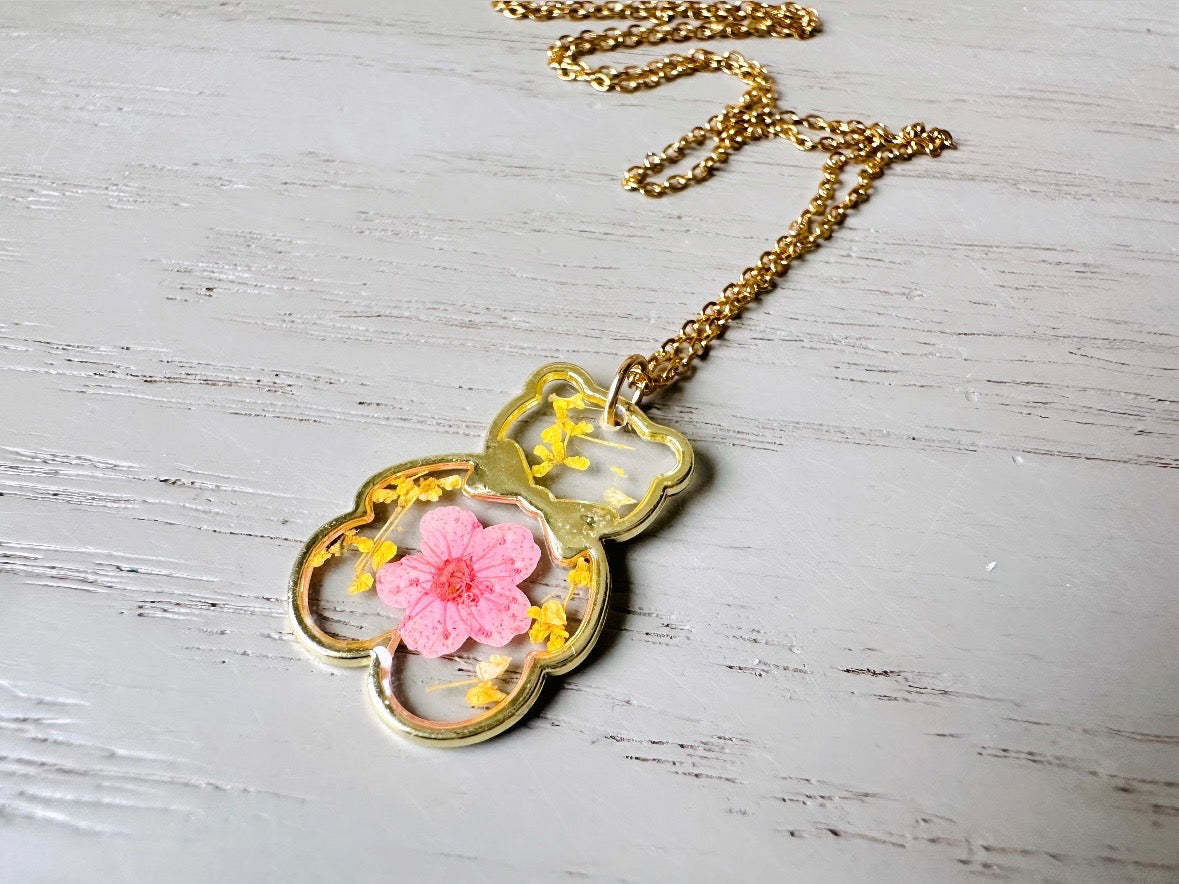 An adorable handmade teddy bear necklace . The necklace is made of 18kt gold and it has a cute teddy bear charm. The charm is clear with pink and yellow real pressed flowers. The bear is trimmed in gold and has a little gold bowtie.