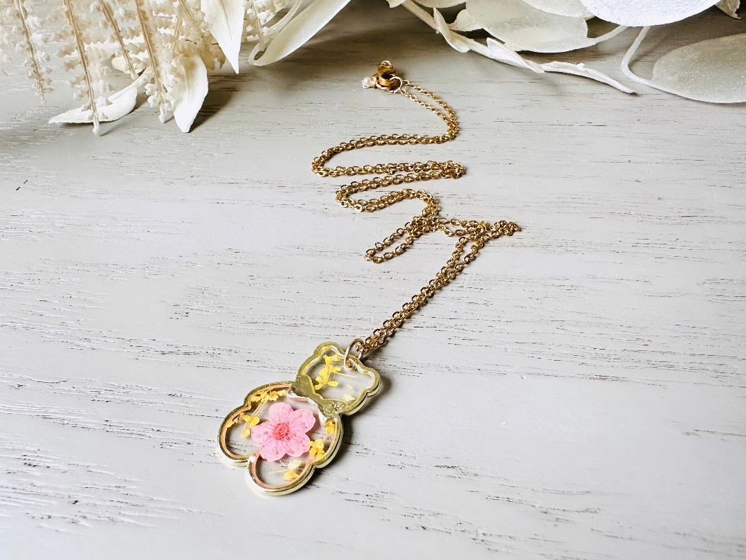 An adorable handmade teddy bear necklace. The necklace is made of 18kt gold and it has a cute teddy bear charm. The charm is clear with pink and yellow real pressed flowers. The bear is trimmed in gold and has a little gold bowtie.