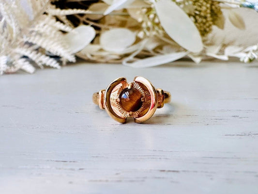 Vintage 14kt gold ring with a genuine Tiger's Eye gemstone, featuring an intricate halo design, displayed on a white surface with decorative flowers.