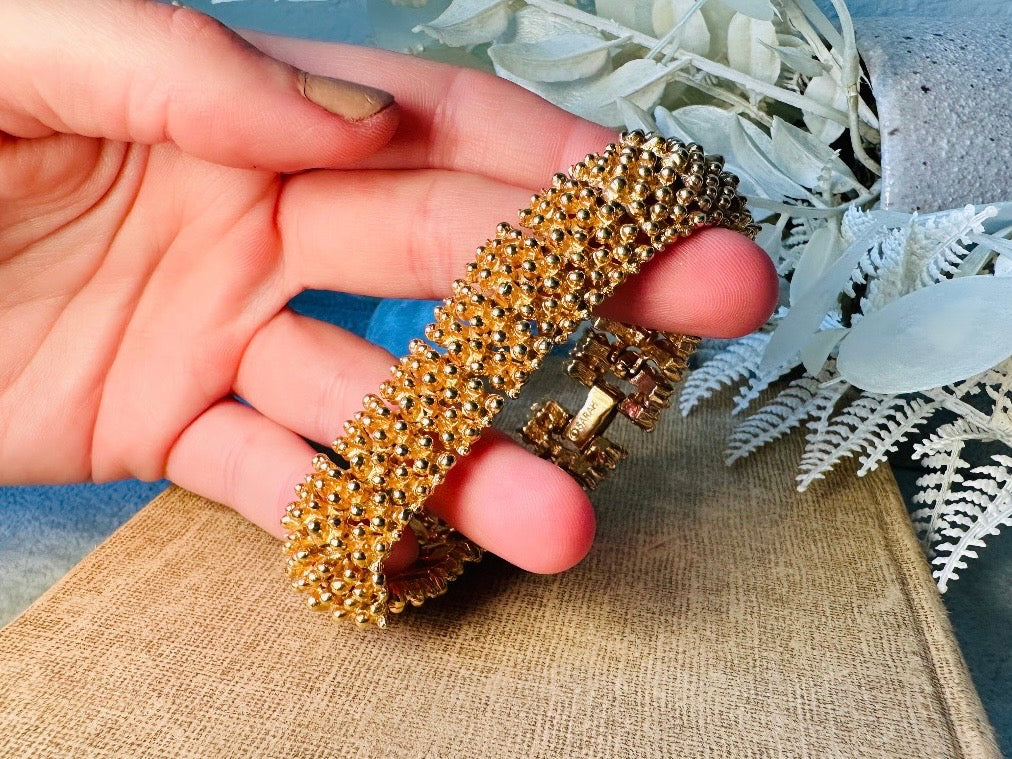 This vintage articulated chunky gold panel bracelet is a showstopper. This signed SC bracelet features articulated gold plated panels with a raised stipple texture throughout. Incredibly well made an in excellent vintage condition. Fastens with a fold over hinge clasp and looks incredible on its own or paired with others for a sensational stack. No flaws to note, please see all pics, from 1973.

Dimensions: 7.75" long, 0.75" wide. Fold over clasp closure.