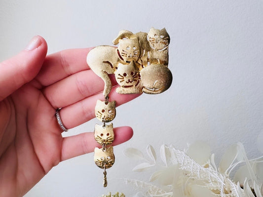 This is a big gold vintage 1980s cat brooch featuring three cats huddled together and three cat heads dangling from their tail. The gold is a classic semi- matte shade with brushed detailing. It is a signed Ultra Craft piece in excellent vintage condition. 