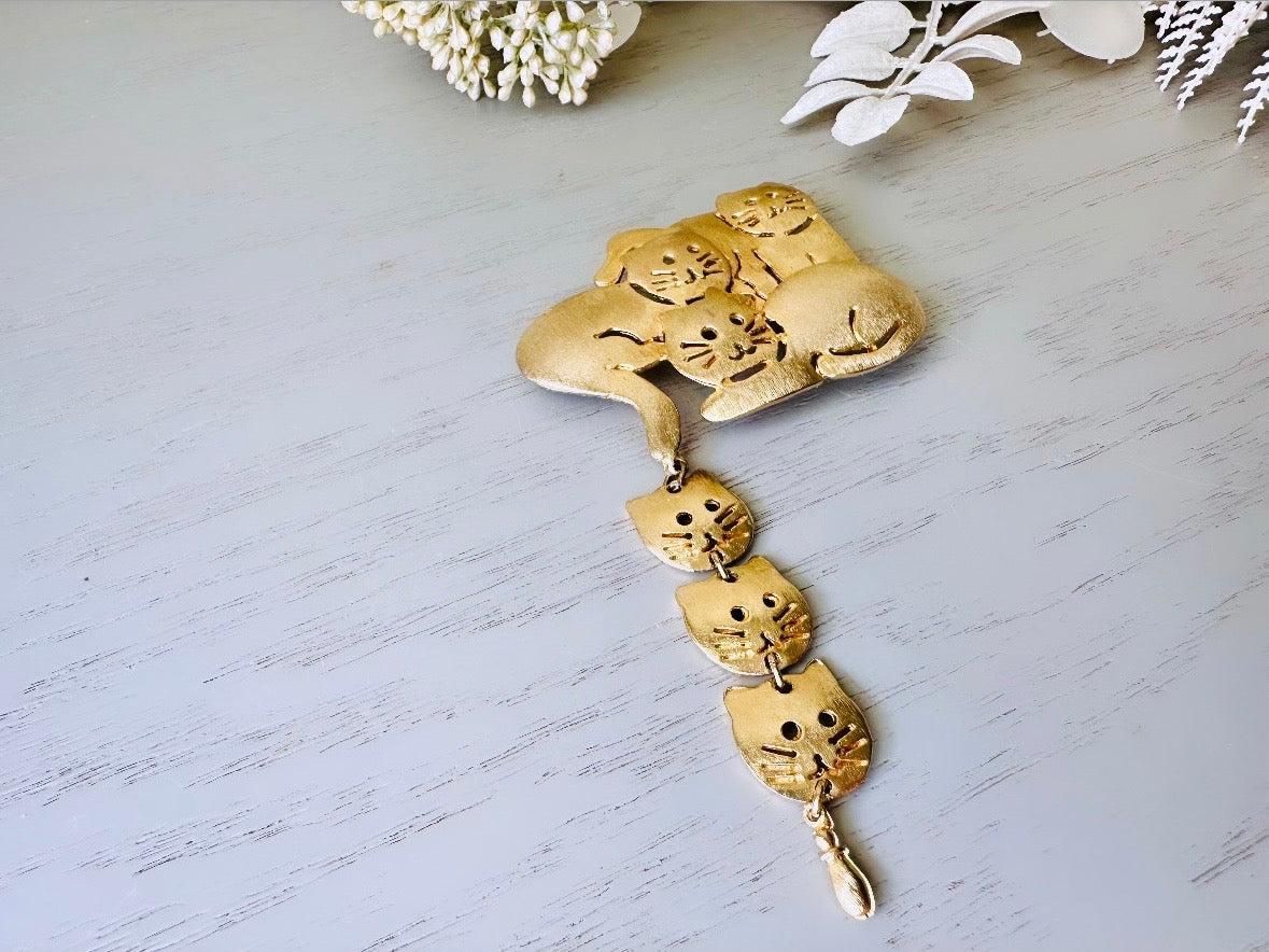 This is a big gold vintage 1980s cat brooch featuring three cats huddled together and three cat heads dangling from their tail. The gold is a classic semi- matte shade with brushed detailing. It is a signed Ultra Craft piece in excellent vintage condition. 