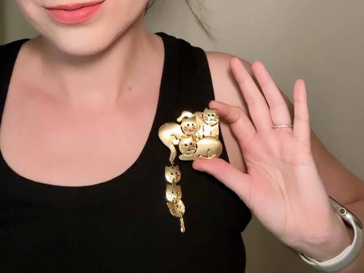 This is a big gold vintage 1980s cat brooch featuring three cats huddled together and three cat heads dangling from their tail. The gold is a classic semi- matte shade with brushed detailing. It is a signed Ultra Craft piece in excellent vintage condition. 