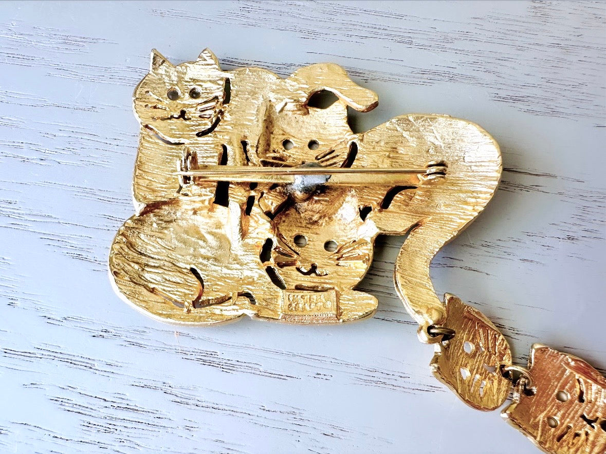 This is a big gold vintage 1980s cat brooch featuring three cats huddled together and three cat heads dangling from their tail. The gold is a classic semi- matte shade with brushed detailing. It is a signed Ultra Craft piece in excellent vintage condition. 