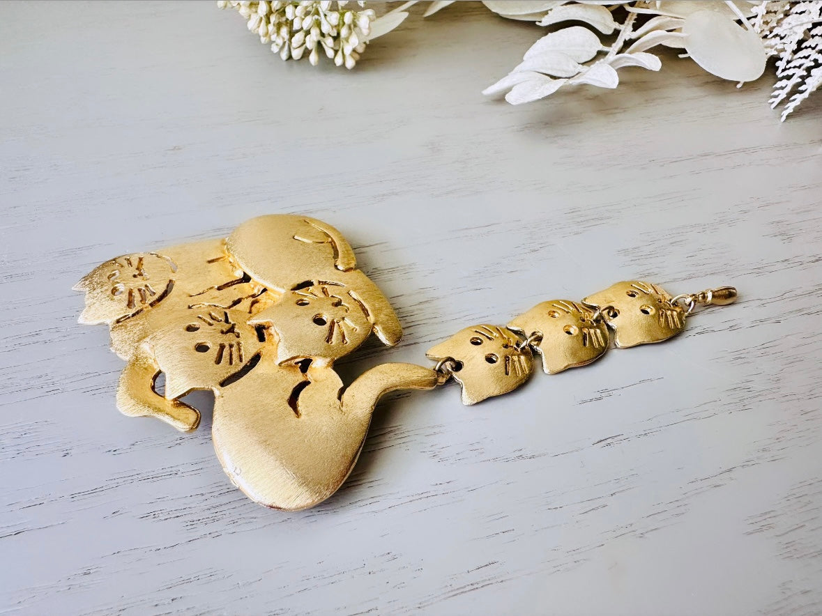 This is a big gold vintage 1980s cat brooch featuring three cats huddled together and three cat heads dangling from their tail. The gold is a classic semi- matte shade with brushed detailing. It is a signed Ultra Craft piece in excellent vintage condition. 