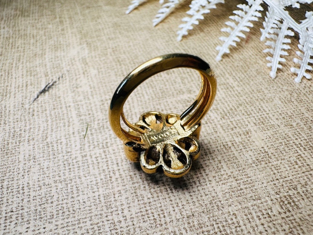 This vintage emerald green and pearl gold cocktail ring is such a pretty piece. Vintage Avon from the 1976 Versailles collection. Green, pearls and gold are a beautiful color combination. The center faceted oval green stone is surrounded in a raised filigree design that is full of vintage character, with two tiny pearl cabochon accents. Signed in excellent vintage condition.&nbsp;