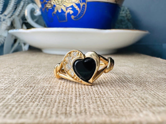 Gold ring with a black heart stone on a textured surface with a blue teacup in the background.