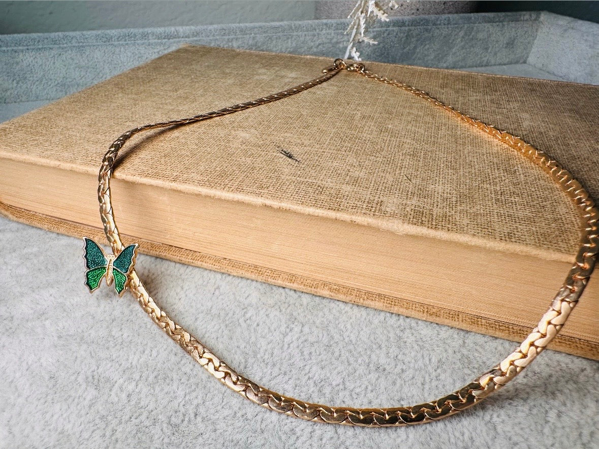This vintage green and gold shy butterfly necklace is an absolute beauty from the 1970s. Elegantly designed to be worn with the butterfly charm on the right side, this dainty choker necklace is so lovely. The chain is a delicate classic gold herringbone chain, the butterfly is two toned in deep green and teal enamel with a pearlized shimmer. Arrives wrapped beautifully and ready to gift to the butterfly lover in your life. &nbsp;An excellent gift or a thoughtful keepsake for a friend. 