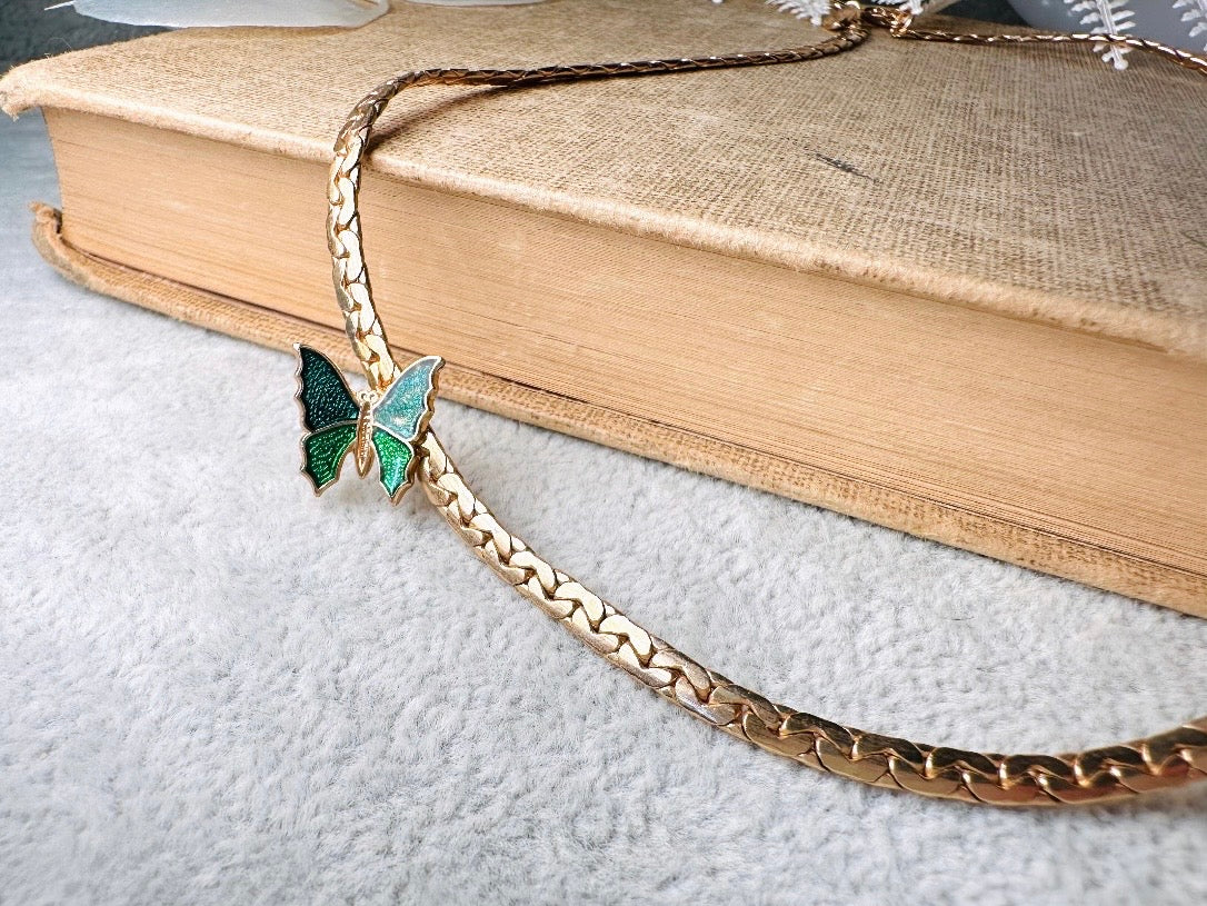 This vintage green and gold shy butterfly necklace is an absolute beauty from the 1970s. Elegantly designed to be worn with the butterfly charm on the right side, this dainty choker necklace is so lovely. The chain is a delicate classic gold herringbone chain, the butterfly is two toned in deep green and teal enamel with a pearlized shimmer. Arrives wrapped beautifully and ready to gift to the butterfly lover in your life. &nbsp;An excellent gift or a thoughtful keepsake for a friend. 