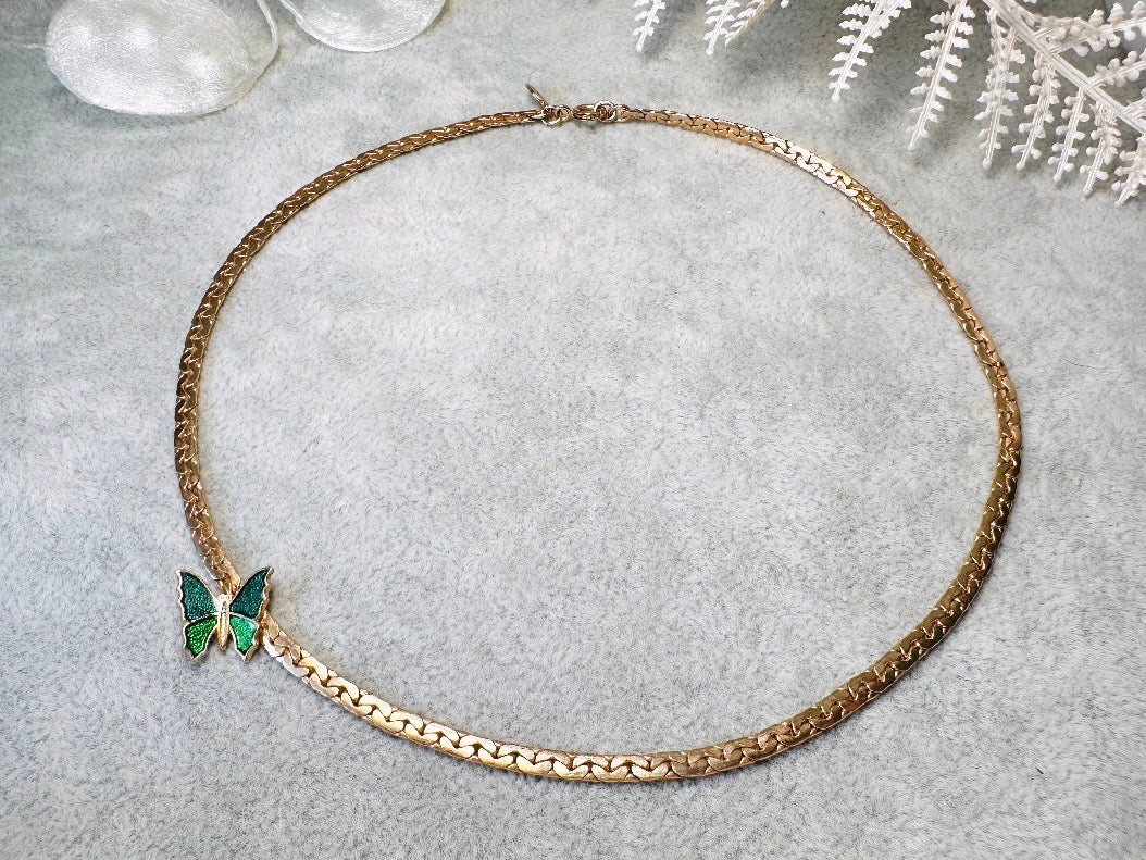 This vintage green and gold shy butterfly necklace is an absolute beauty from the 1970s. Elegantly designed to be worn with the butterfly charm on the right side, this dainty choker necklace is so lovely. The chain is a delicate classic gold herringbone chain, the butterfly is two toned in deep green and teal enamel with a pearlized shimmer. Arrives wrapped beautifully and ready to gift to the butterfly lover in your life. &nbsp;An excellent gift or a thoughtful keepsake for a friend. 