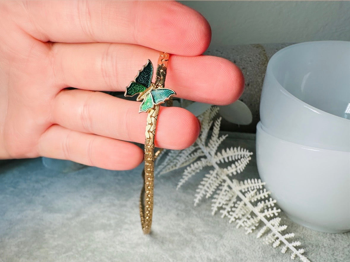 This vintage green and gold shy butterfly necklace is an absolute beauty from the 1970s. Elegantly designed to be worn with the butterfly charm on the right side, this dainty choker necklace is so lovely. The chain is a delicate classic gold herringbone chain, the butterfly is two toned in deep green and teal enamel with a pearlized shimmer. Arrives wrapped beautifully and ready to gift to the butterfly lover in your life. &nbsp;An excellent gift or a thoughtful keepsake for a friend. 