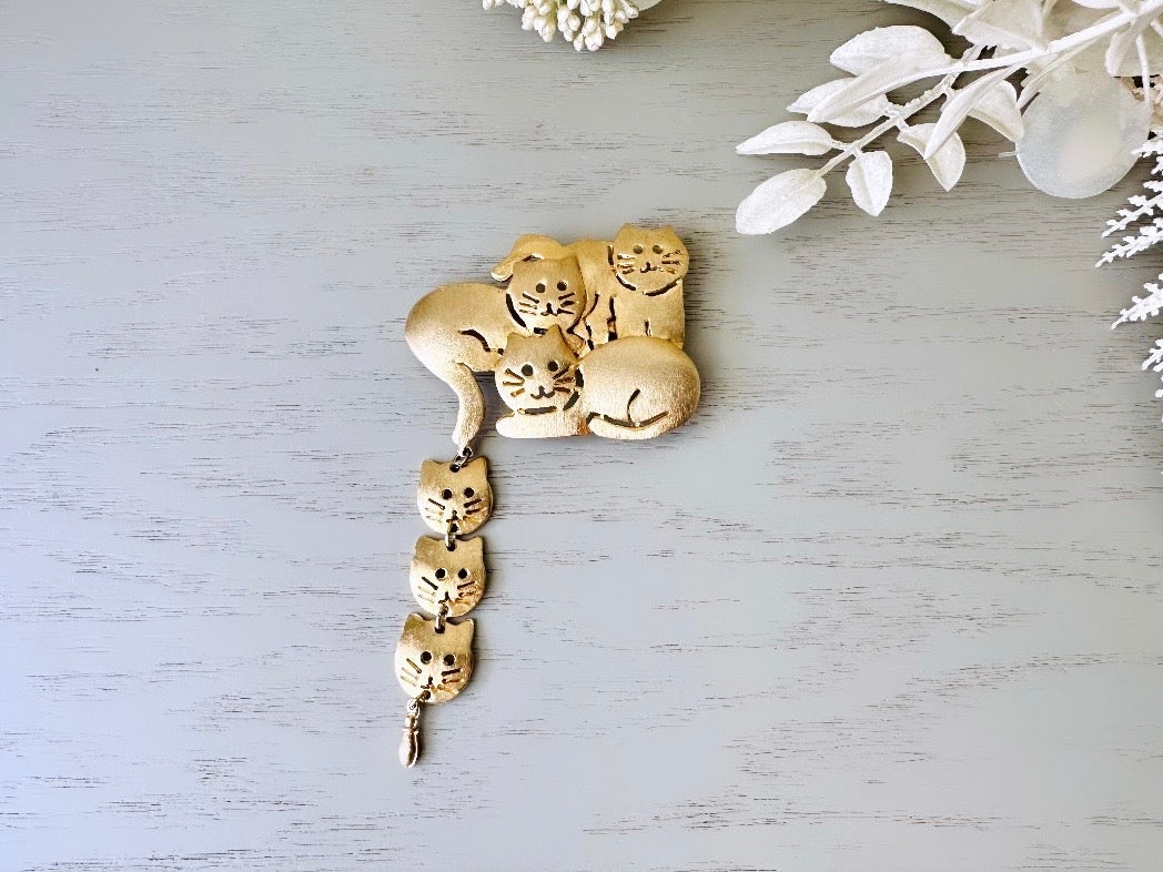 This is a big gold vintage 1980s cat brooch featuring three cats huddled together and three cat heads dangling from their tail. The gold is a classic semi- matte shade with brushed detailing. It is a signed Ultra Craft piece in excellent vintage condition. 