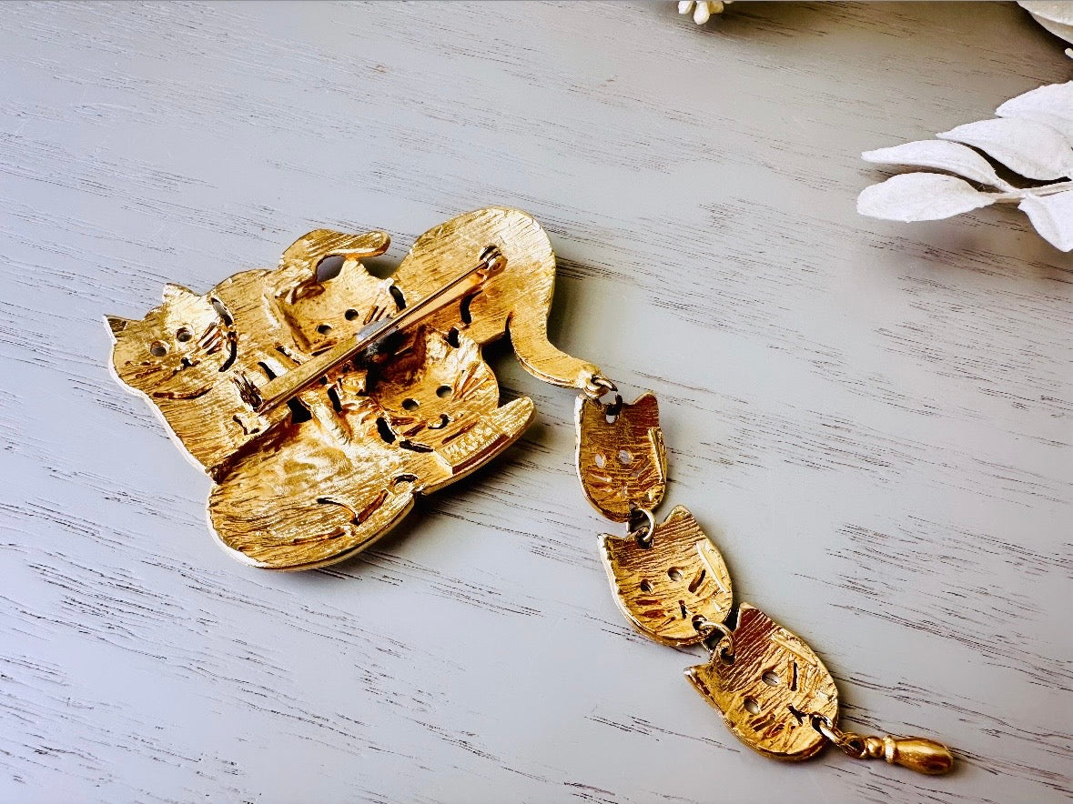 This is a big gold vintage 1980s cat brooch featuring three cats huddled together and three cat heads dangling from their tail. The gold is a classic semi- matte shade with brushed detailing. It is a signed Ultra Craft piece in excellent vintage condition. 