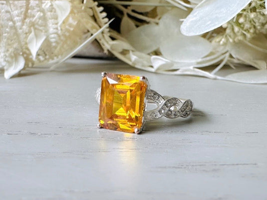 This sparkling vintage Citrine statement ring is gorgeous. Featuring a large honey yellow emerald cut stone prong set in a silver base. The band has tiny cubic zirconias set in the interwoven scroll pattern. Signed Natalia V Collister (NVC). Great vintage condition, very minor wear- please see pics. A beautiful addition to your vintage jewelry collection.

Dimensions: fitted ring, US size 10