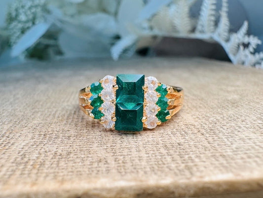 This vintage cocktail ring features a stunning art deco design with brilliant emerald green stacked princess cut rhinestones flanked with dazzling cubic zirconias and tiny green stones. Prong set in a 14K gold-plated base, this fitted size 7 ring is a beautiful and timeless vintage piece. The glass crystals catch the light beautifully and are full of sparkle. This vintage ring will arrive beautifully packaged and ready to gift, or to keep as a treat to yourself.