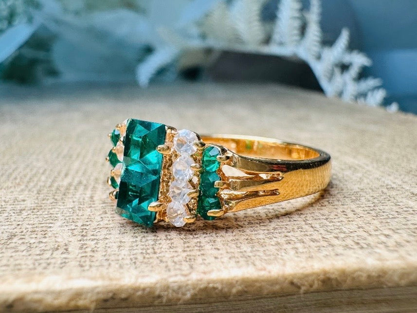 This vintage cocktail ring from Piggle and Pop features a stunning art deco design with brilliant emerald green stacked princess cut rhinestones flanked with dazzling cubic zirconias and tiny green stones. Prong set in a 14K gold-plated base, this fitted size 7 ring is a beautiful and timeless vintage piece. The glass crystals catch the light beautifully and are full of sparkle. This vintage ring will arrive beautifully packaged and ready to gift, or to keep as a treat to yourself.