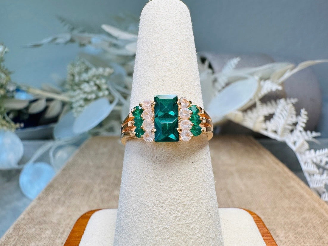 This vintage cocktail ring from Piggle and Pop features a stunning art deco design with brilliant emerald green stacked princess cut rhinestones flanked with dazzling cubic zirconias and tiny green stones. Prong set in a 14K gold-plated base, this fitted size 7 ring is a beautiful and timeless vintage piece. The glass crystals catch the light beautifully and are full of sparkle.