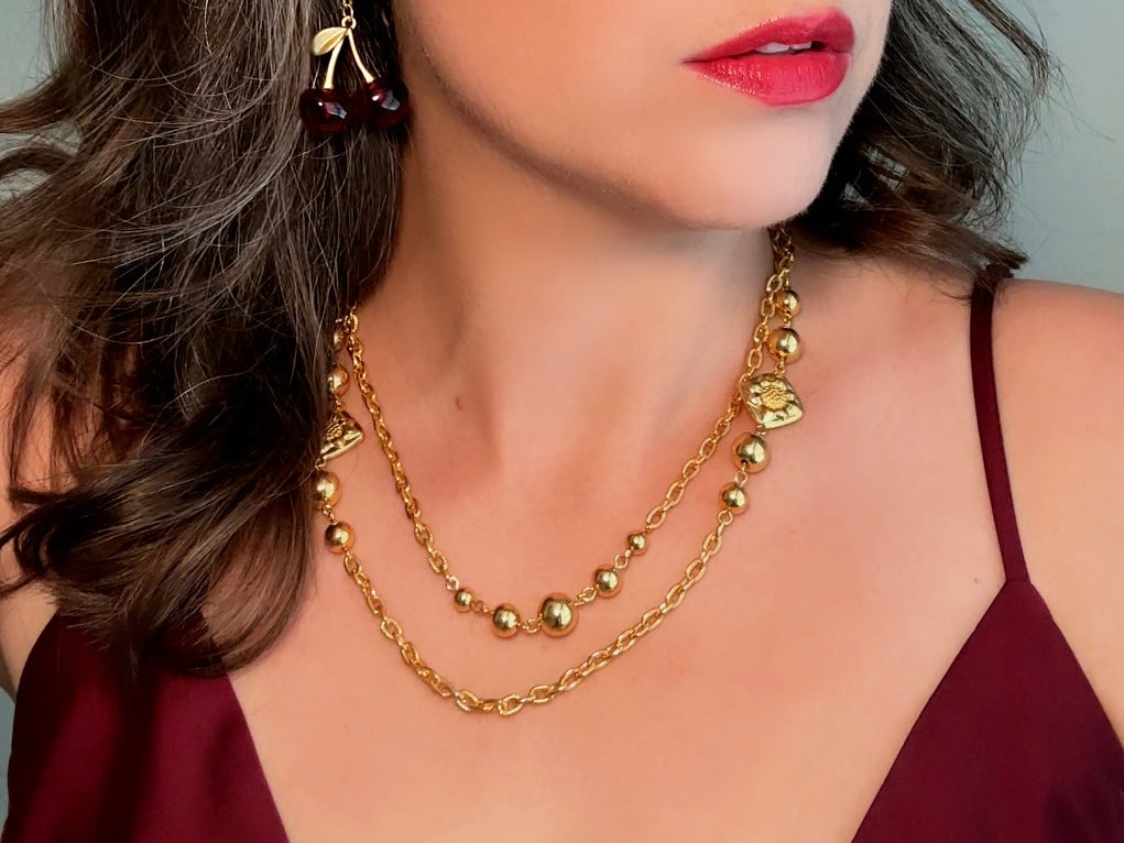 This vintage double strand Liz Claiborne gold chain necklace is a beautifully unique find. Featuring two strands of shimmering gold chain already perfectly layered- with graduated gold balls in varying sizes and Etruscan floral accents. Signed with signature LCI triangle hang tag on the end of extender chain. Versatile while making a statement, and incredibly flattering. Excellent vintage condition.