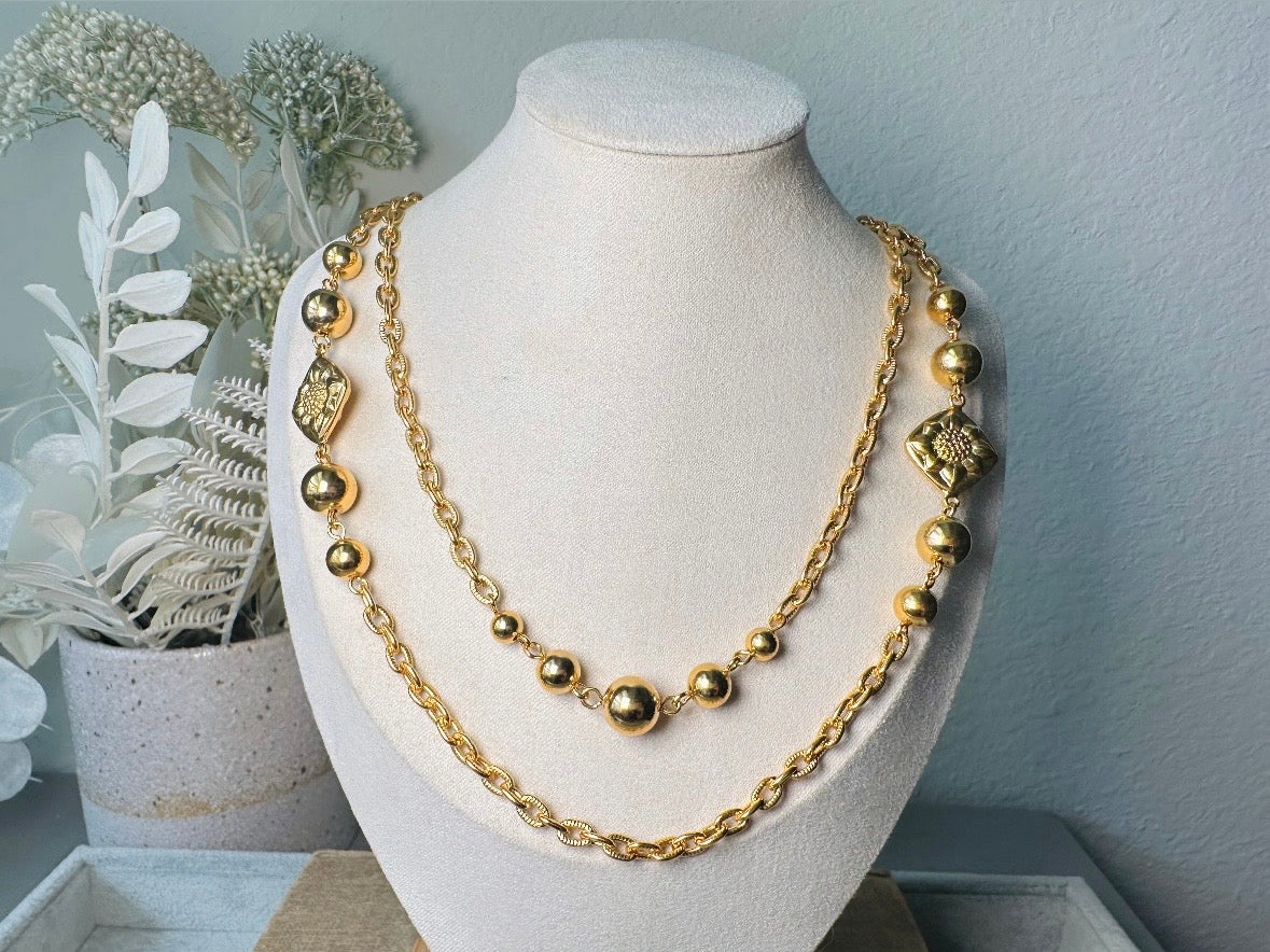 This vintage double strand Liz Claiborne gold chain necklace is a beautifully unique find. Featuring two strands of shimmering gold chain already perfectly layered- with graduated gold balls in varying sizes and Etruscan floral accents. Signed with signature LCI triangle hang tag on the end of extender chain. Versatile while making a statement, and incredibly flattering. Excellent vintage condition.
