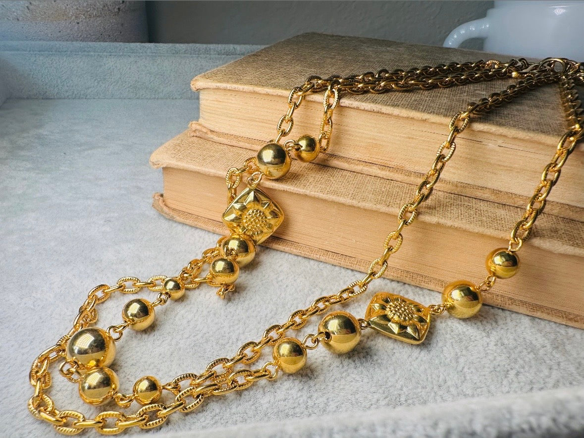 This vintage double strand Liz Claiborne gold chain necklace is a beautifully unique find. Featuring two strands of shimmering gold chain already perfectly layered- with graduated gold balls in varying sizes and Etruscan floral accents. Signed with signature LCI triangle hang tag on the end of extender chain. Versatile while making a statement, and incredibly flattering. Excellent vintage condition.