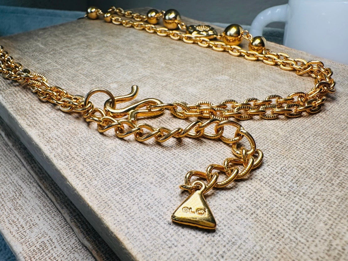 This vintage double strand Liz Claiborne gold chain necklace is a beautifully unique find. Featuring two strands of shimmering gold chain already perfectly layered- with graduated gold balls in varying sizes and Etruscan floral accents. Signed with signature LCI triangle hang tag on the end of extender chain. Versatile while making a statement, and incredibly flattering. Excellent vintage condition.