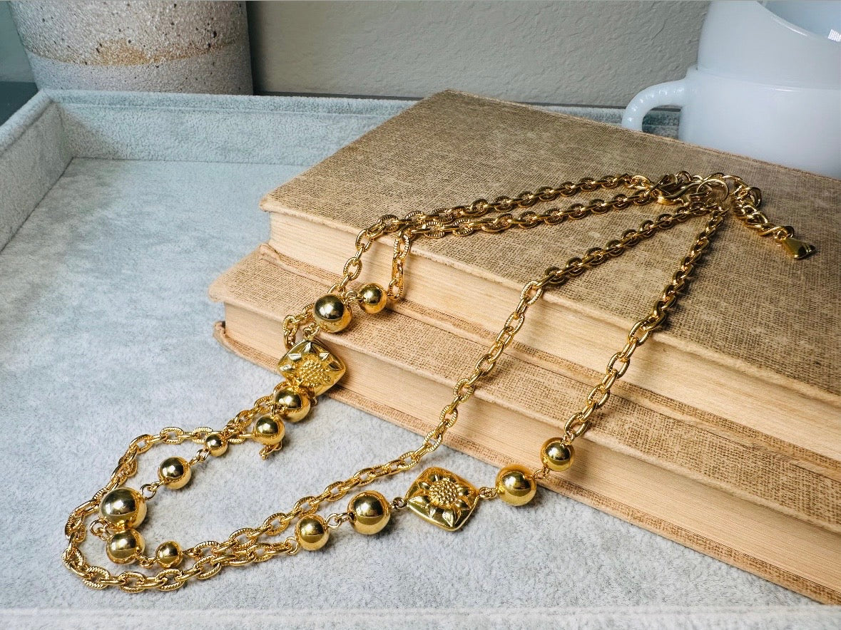 This vintage double strand Liz Claiborne gold chain necklace is a beautifully unique find. Featuring two strands of shimmering gold chain already perfectly layered- with graduated gold balls in varying sizes and Etruscan floral accents. Signed with signature LCI triangle hang tag on the end of extender chain. Versatile while making a statement, and incredibly flattering. Excellent vintage condition.