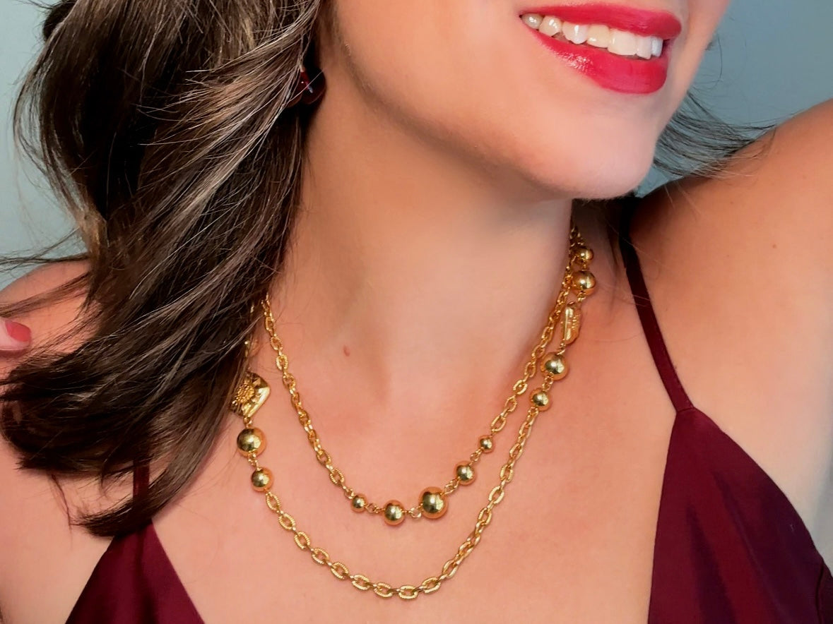 This vintage double strand Liz Claiborne gold chain necklace is a beautifully unique find. Featuring two strands of shimmering gold chain already perfectly layered- with graduated gold balls in varying sizes and Etruscan floral accents. Signed with signature LCI triangle hang tag on the end of extender chain. Versatile while making a statement, and incredibly flattering. Excellent vintage condition.