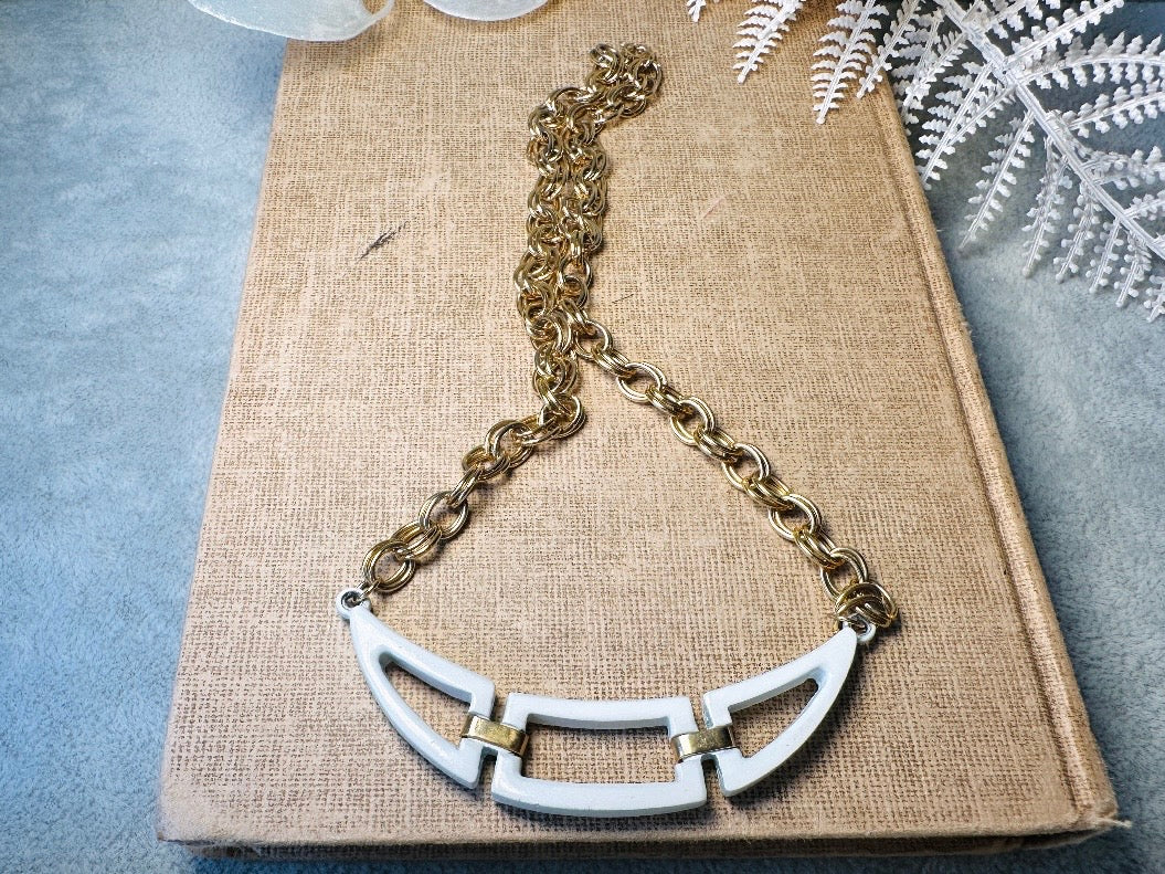 This white and gold vintage geometric necklace is chic and unique. Double link gold curb chain connects with a white geometric pendant bib, comprised or three white enameled articulated pieces. Versatile while making a statement. Minimal wear and in great vintage condition. A perfect summer necklace to incorporate into a variety of looks, paired with others or worn alone.

Dimensions:  18" long
