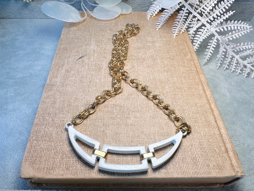 This white and gold vintage geometric necklace is chic and unique. Double link gold curb chain connects with a white geometric pendant bib, comprised or three white enameled articulated pieces. Versatile while making a statement. Minimal wear and in great vintage condition. A perfect summer necklace to incorporate into a variety of looks, paired with others or worn alone.

Dimensions:  18" long