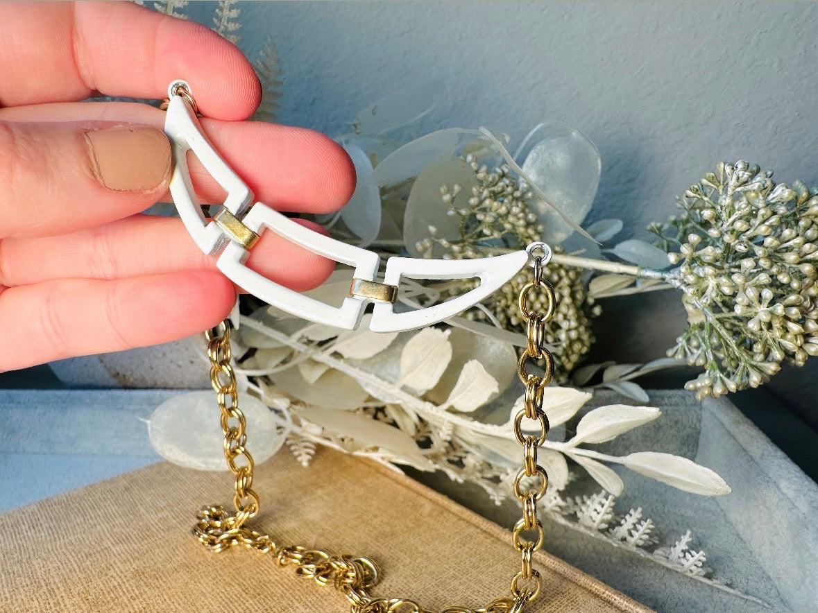This white and gold vintage geometric necklace is chic and unique. Double link gold curb chain connects with a white geometric pendant bib, comprised or three white enameled articulated pieces. Versatile while making a statement. Minimal wear and in great vintage condition. A perfect summer necklace to incorporate into a variety of looks, paired with others or worn alone.

Dimensions:  18" long