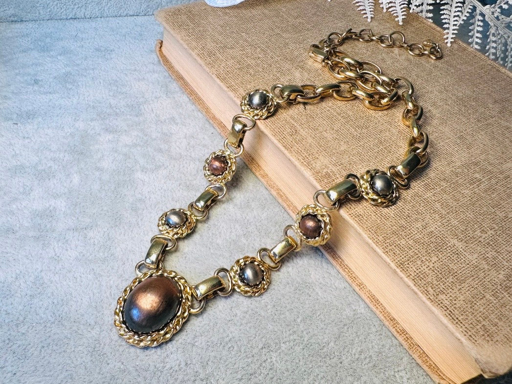 This vintage Etruscan style Liz Claiborne gold chain necklace is a beautifully unique find. Featuring large curb chain links with round cabochons of faux hematite and bronze set in gold bezels. In the center is a larger bronzed oval cabochon in the same style of gold roped bezel. Signed on back of center cabochon as well as the signature LCI triangle hang tag on the end of extender chain. Versatile while making a statement, and incredibly flattering. Minimal wear from age, no major flaws to note; &nbsp;in g