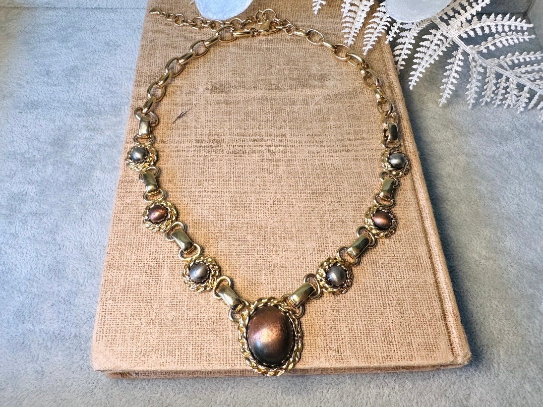 This vintage Etruscan style Liz Claiborne gold chain necklace is a beautifully unique find. Featuring large curb chain links with round cabochons of faux hematite and bronze set in gold bezels. In the center is a larger bronzed oval cabochon in the same style of gold roped bezel. Signed on back of center cabochon as well as the signature LCI triangle hang tag on the end of extender chain. Versatile while making a statement, and incredibly flattering. Minimal wear from age, no major flaws to note; &nbsp;in g